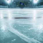 Leere, glänzende Eisfläche in einer hell beleuchteten Eissporthalle mit Banden und Schutznetzen im Hintergrund
